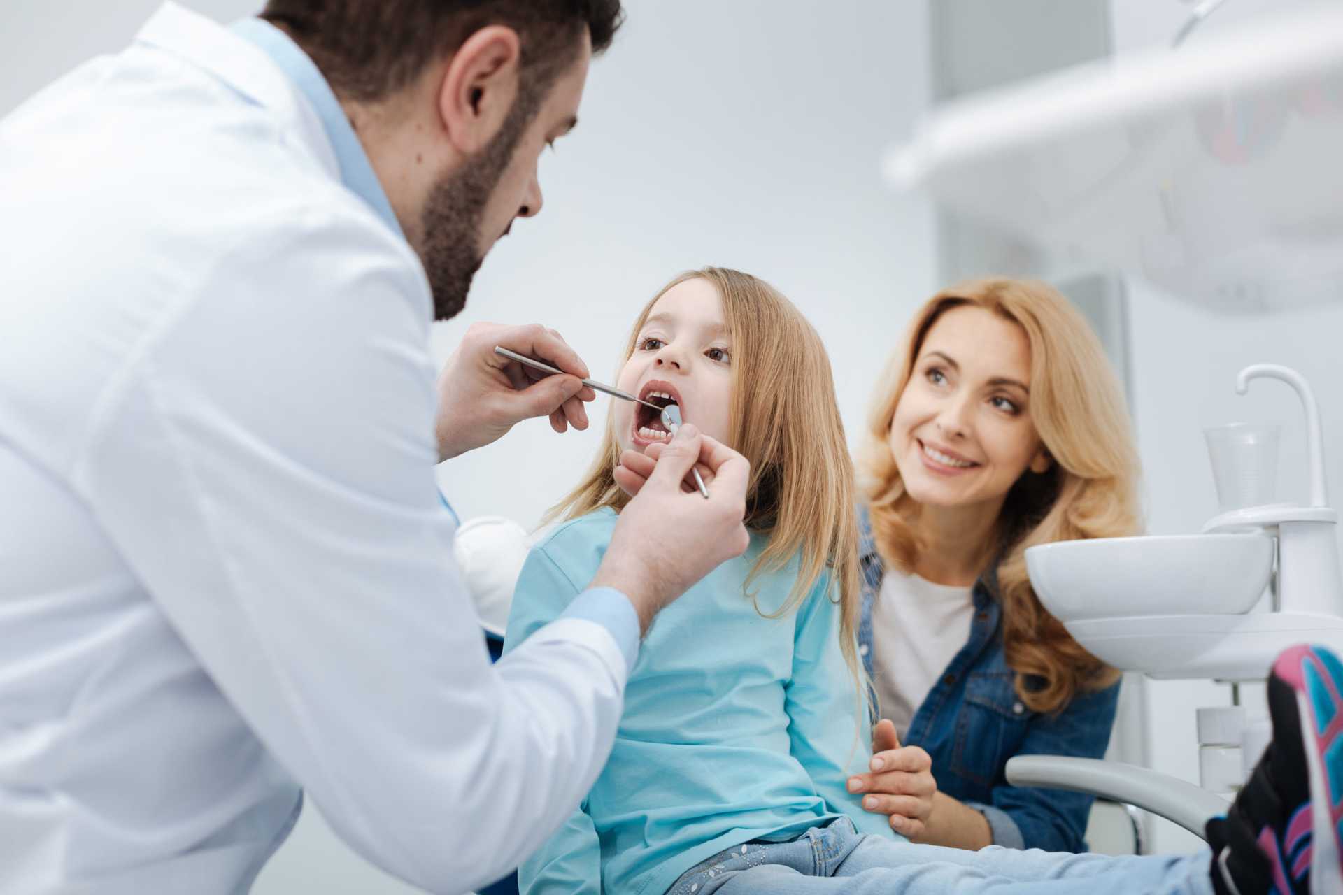 Woman sitting behind girl with mouth open and Dr inspecting teeth