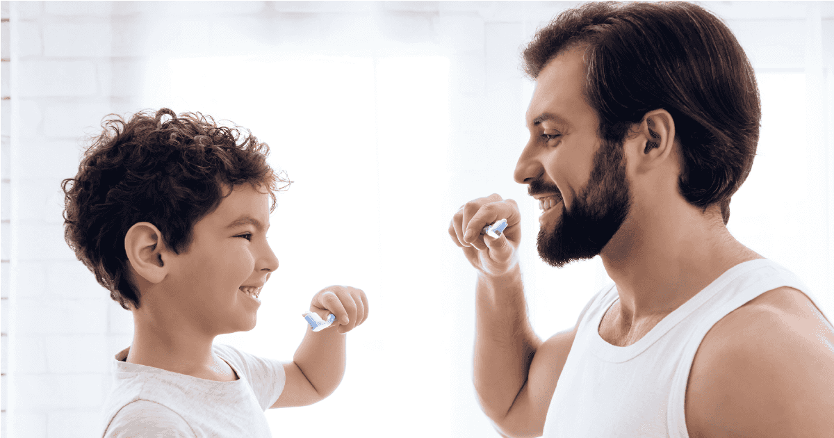 Man and boy both holding toothbrushes in front of mouths