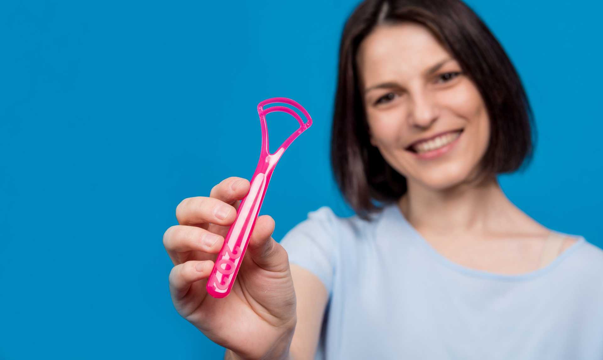 Beautiful,happy,young,woman,with,tongue,scraper,on,blank,blue