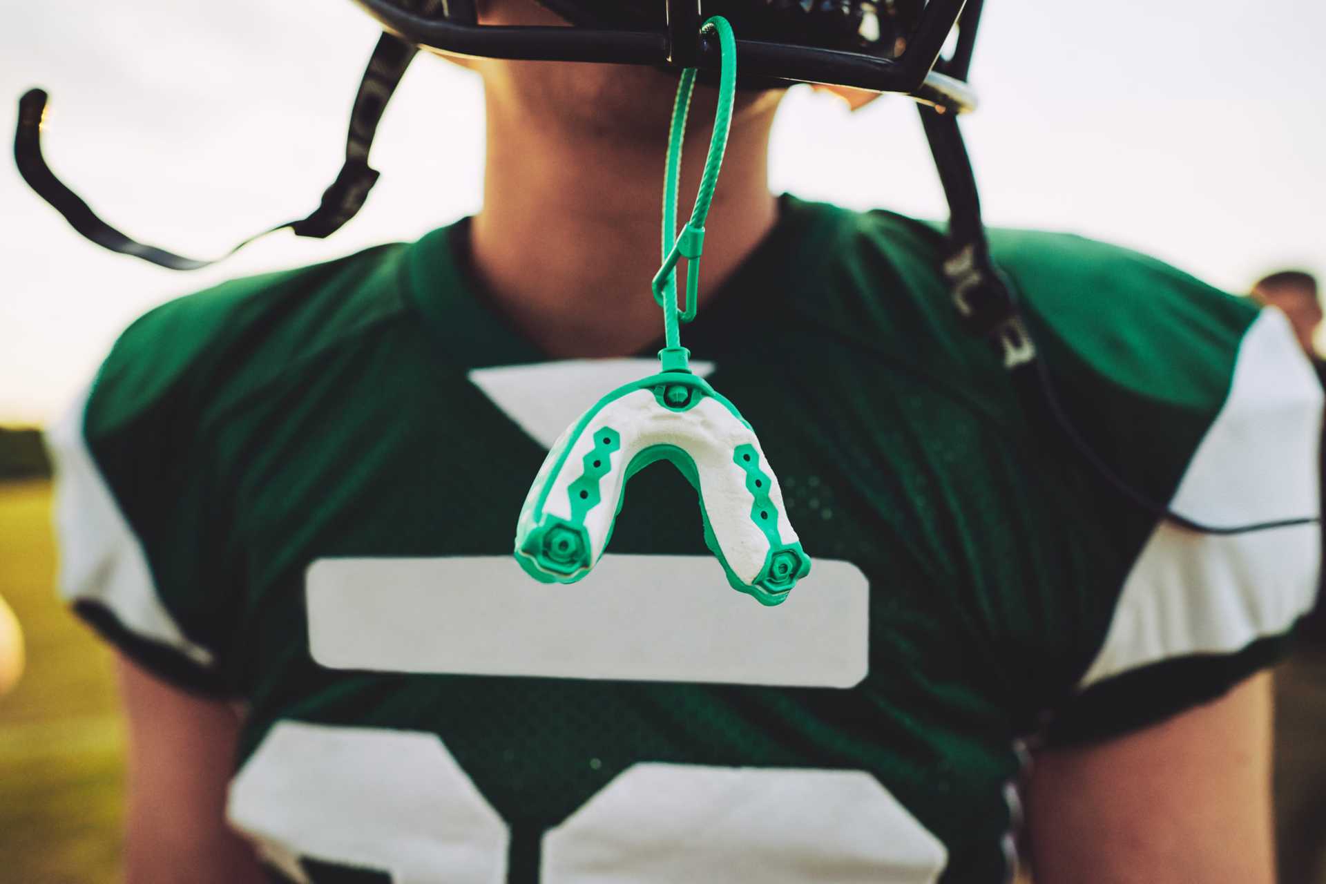 Boy in football jersey wearing helmet with mouth guard hanging down